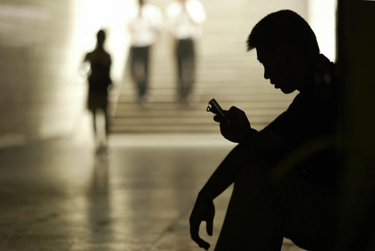 In silhouette, a man looks at his mobile phone.