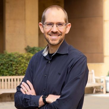 A photo of Stephen Schueller, executive director of PsyberGuide, wearing a dark blue button down shirt and smiling at the camera.