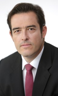 A portrait of Volker Treier in a suit and red tie.