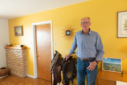 Raymond Skiles standing in a bright yellow room next to a saddle. 