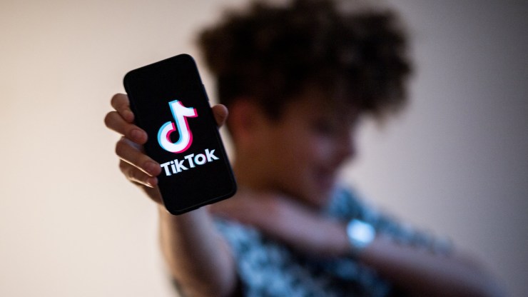 A teenager holds a phone that shows the logo for TikTok.
