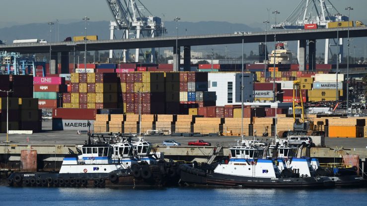 Tug boats in front of containers stacked at a port.