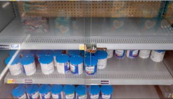Sparsely stocked shelves of baby formula locked in a glass case at a grocery store.