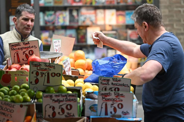 A customer pays for his fruit and vegetables with a ten pound sterling note, at a trader's market stall in London on May 12, 2022. - Britain's economy shrank in March on fallout from soaring inflation, increasing the prospect of the country falling into recession. Official first-quarter data on Thursday showed that following solid output in January, the UK economy posted zero growth the following month and contracted by 0.1 percent in March.