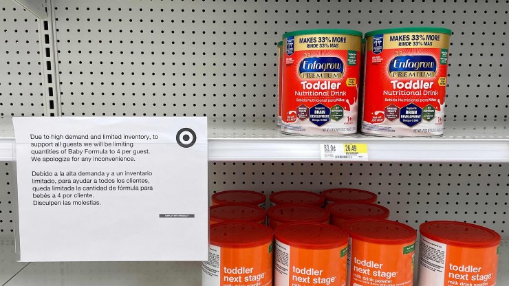 A sign letting customers know that there is a limit on how many cans of baby formula can be purchased is seen in front of sparsely stocked shelves.
