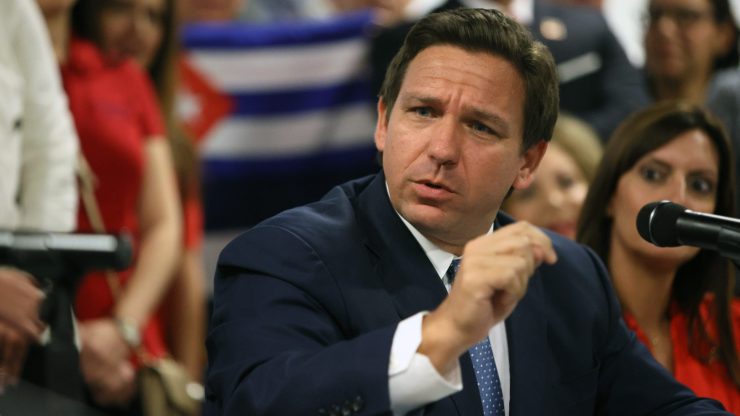 Gov. Ron DeSantis holds his hand up as he speaks to someone at a table.