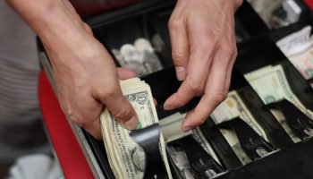 A person handling dollar bills in a cash register.