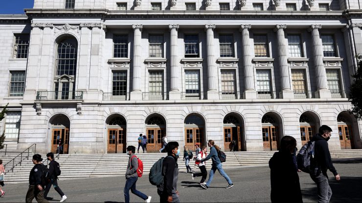 College students walking on campus on a sunny day in front of a large columned building.
