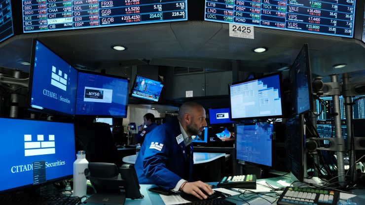Person sitting at the New York Stock Exchange with screens in the background.