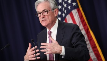Federal Reserve Chair Jerome Powell stands at a podium, moving his hands as he speaks.
