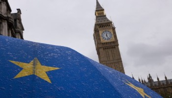 An umbrella bearing the EU flag glimmers with rain in front of Big Ben.