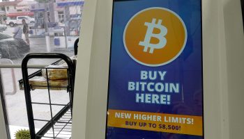 A bitcoin ATM at a store, with the phrase "BUY BITCOIN HERE!" on the screen.
