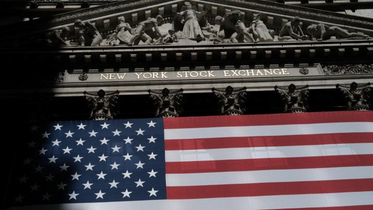The exterior of the New York Stock Exchange is seen with an American flag draped across the building's columns.