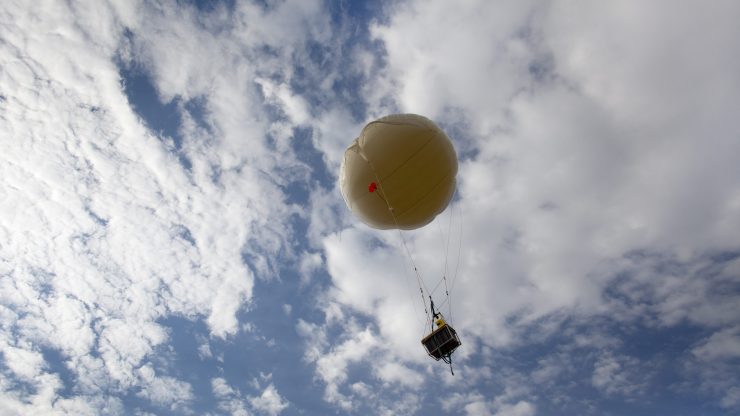 A weather balloon flying on a partly cloudy day.
