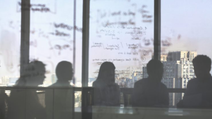 Silhouettes of a group of people in a board room in room facing a city skyline.