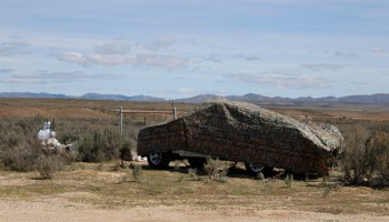 A vehicle is covered by a camouflage tarp on a prairie.
