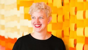 Gretchen Culver smiles for a portrait in front of a wall decorated in orange paper.