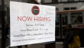 A now hiring sign is posted in a restaurant.