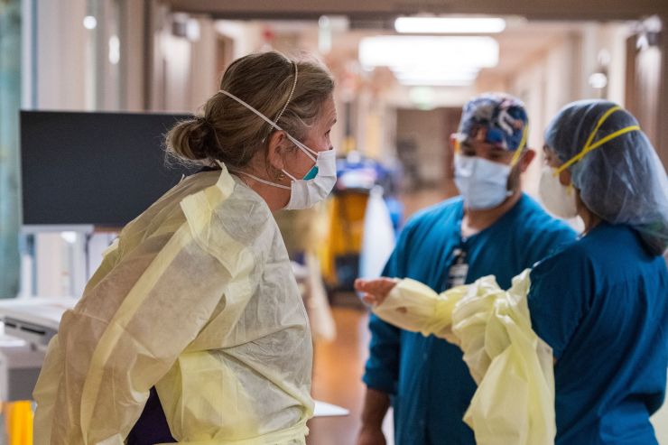 Three nurses stand in a hospital hallway wearing protective gear