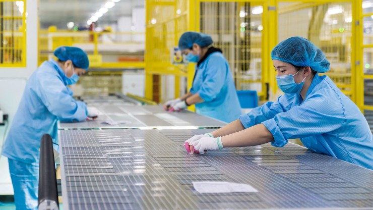 Chinese workers in hairnets and masks produce parts for solar panels.
