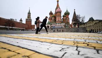 A couple walk in front of the Kremlin's Spasskaya tower and St Basil's cathedral in downtown Moscow on April 17, 2022.