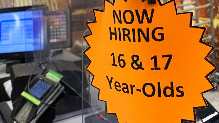 Signage advertising now hiring for 16 and 17 year old employees is displayed on a cash register inside a discount department retail store.
