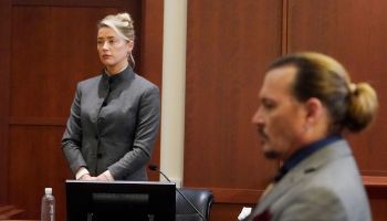 Amber Heard, standing in the background to the left, and Johnny Depp, seated, in a courtroom.