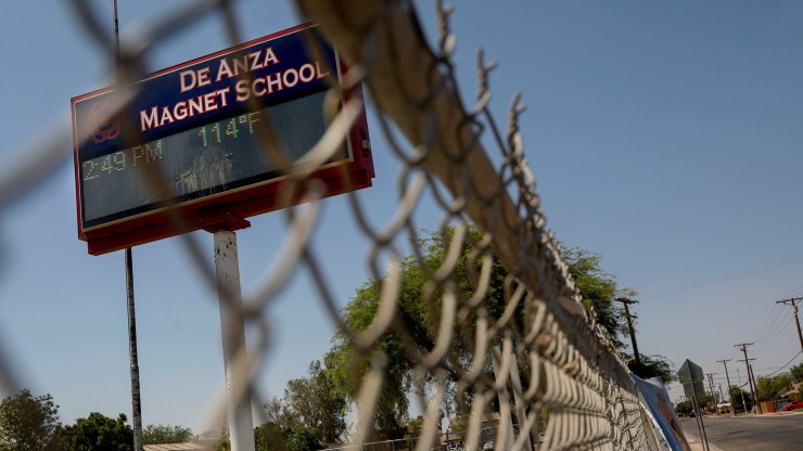 Behind a chain link fence, a sign for De Anza Magnet School in El Centro, California reads 114º.