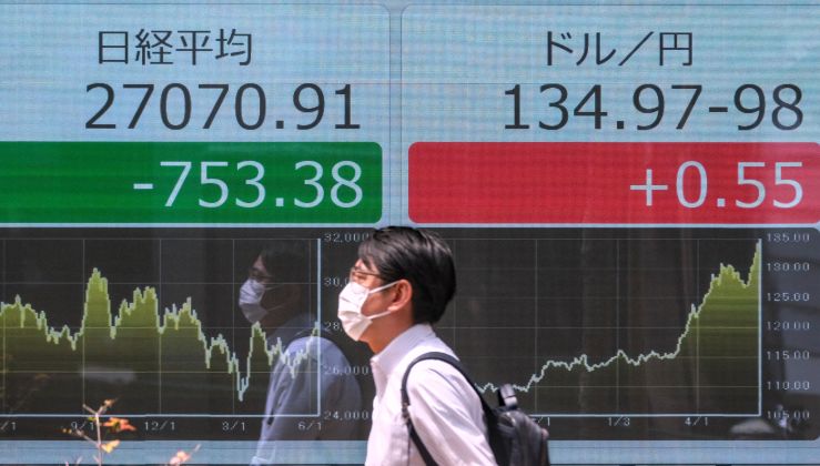 A pedestrian walks past an electronic share price board showing the Tokyo Stock Exchange.