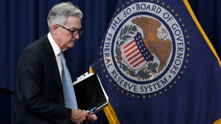 Fed Chair Jerome Powell leaves a press conference and walks past a flag for the Federal Reserve Board of Governors.