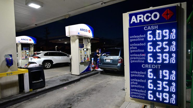 An Arco gas station at night. Two pumps are on the left and a list of gas prices are on the right on a blue sign.