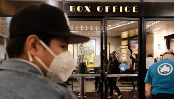 A masked person is seen in front of the Box Office for "The Lion King" at a Broadway theater in New York.