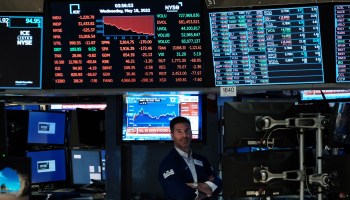 A stock trader is seen on the floor of the New York Stock Exchange. Above him are television screens showing stock trends, with many figures shown in red to indicate a decline in values.