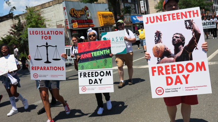 People march during a Juneteenth reparations rally in Newark, New Jersey. They hold signs reading "Freedom Day" and "Legislation for Reparations."