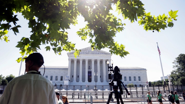 The Supreme Court is seen on a sunny day, behind a fence and cameraman.