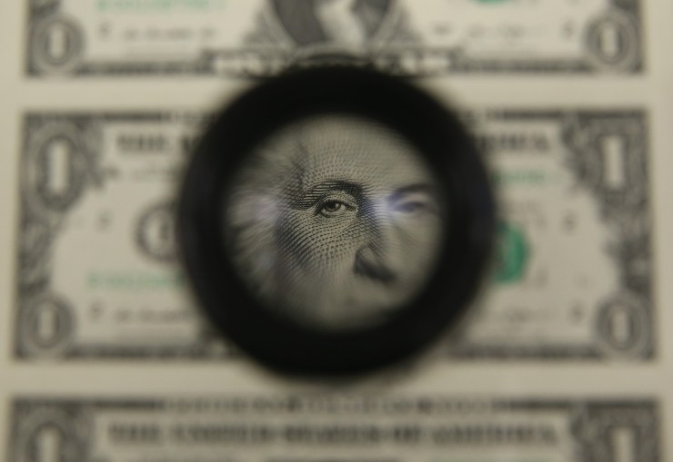 A magnifying glass hovers over the face of George Washington on a sheet of newly printed $1 bills.