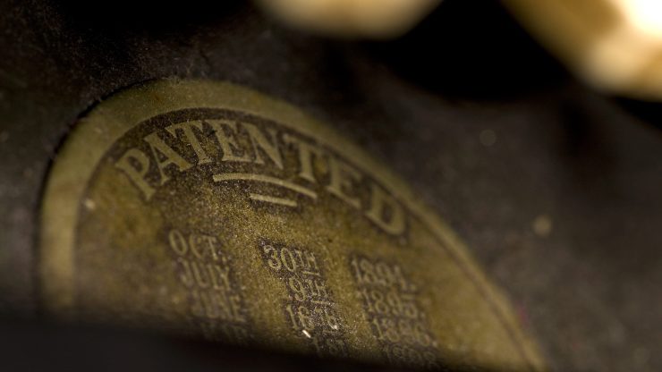 A closeup of the top half of a bronze-colored patent stamp. The visible text says "Patented."