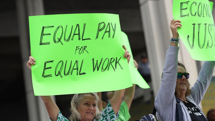 A woman holds a neon poster at protest that reads "Equal pay for equal work."