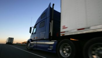 Trucks head east on a highway as the sun rises.