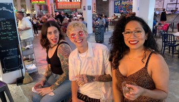 Three people sit at a bar with drinks and smile for a photograph.