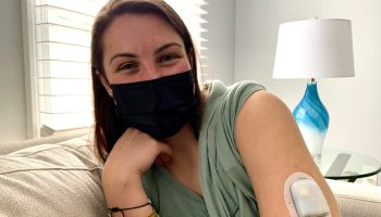 Alina Bills wears a face mask and poses for a picture. Her sleeve is rolled up, exposing the insulin pump she uses.