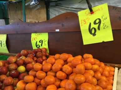 At a market, two cartons of satsuma mandarins are seen. Above them, a sign is posted showing that customers can by them by the kilo or the half pound.