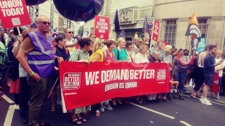 Workers march through London with a banner reading, "We Demand Better. Enough is enough."