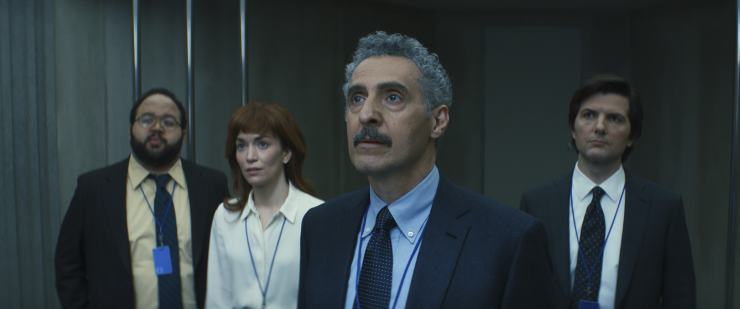 Four office workers wearing suits and other formal attire stare into the distance.