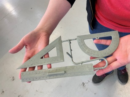 A person holds a ruler, set square and protractor made from recycled masks. They are connected by thin, grey plastic strips.
