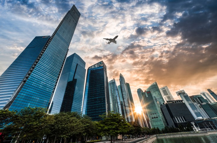Airplane flying over the financial district in Singapore City at sunset.