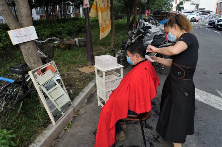 A stylist cuts someone's hair on a street in Shanghai.