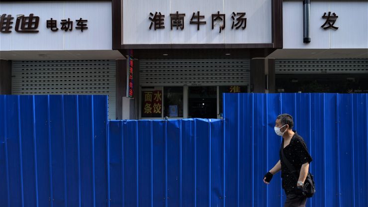 A masked person walks past a boarded-up street in Shanghai.