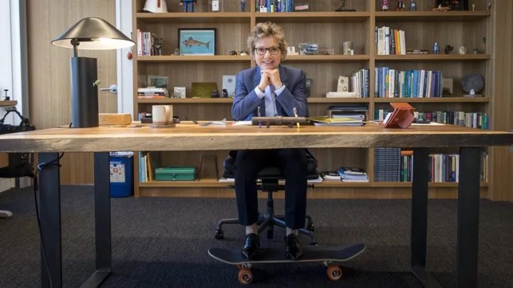 Mary Daly, president of the San Francisco fed, sits at a desk with a bookshelf behind her. Her feet rest on a skateboard.