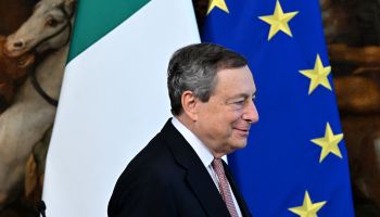 Italian Prime Minister Mario Draghi walks past the Italian and European Union flags.
